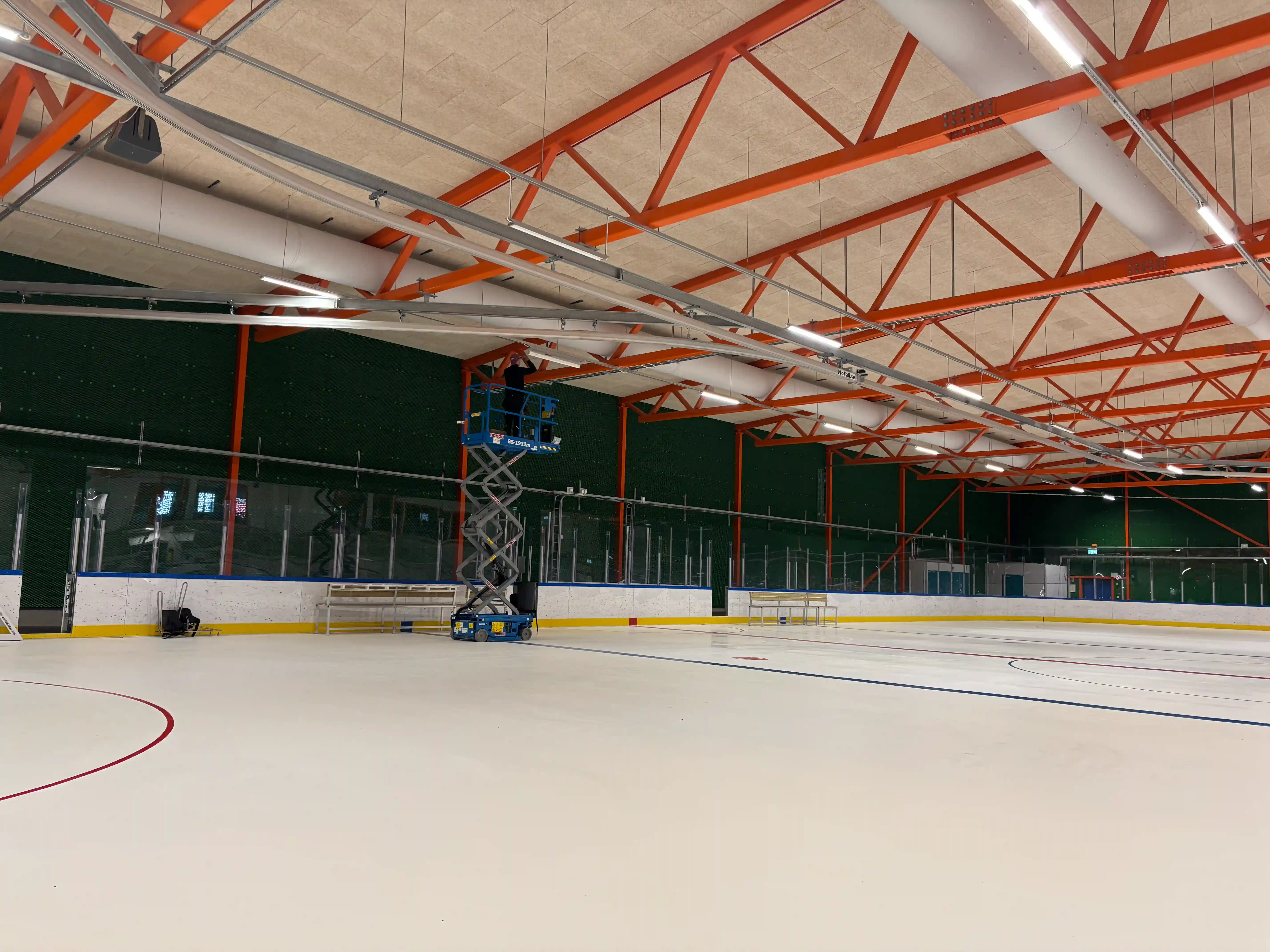 Elektriker monterar puckskydd på armaturer med saxlift i Mälarhöjdens Ishall – AE Elteknik
